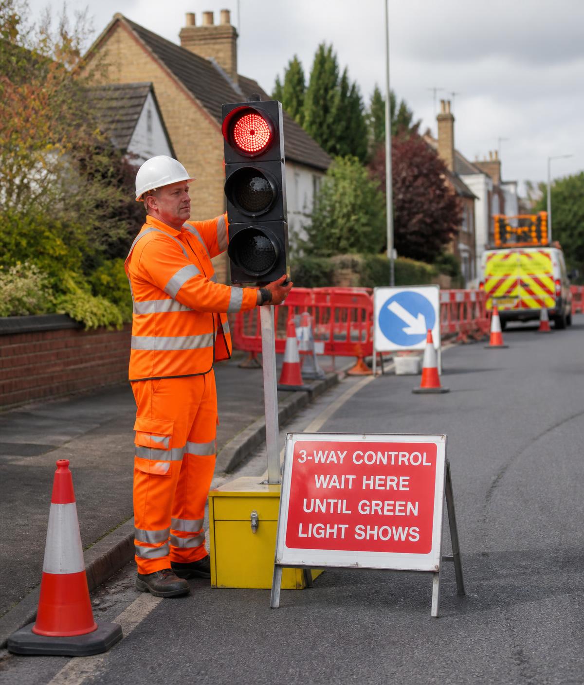 Operative in hi-vis installing portable temporary traffic signals at UK roadworks