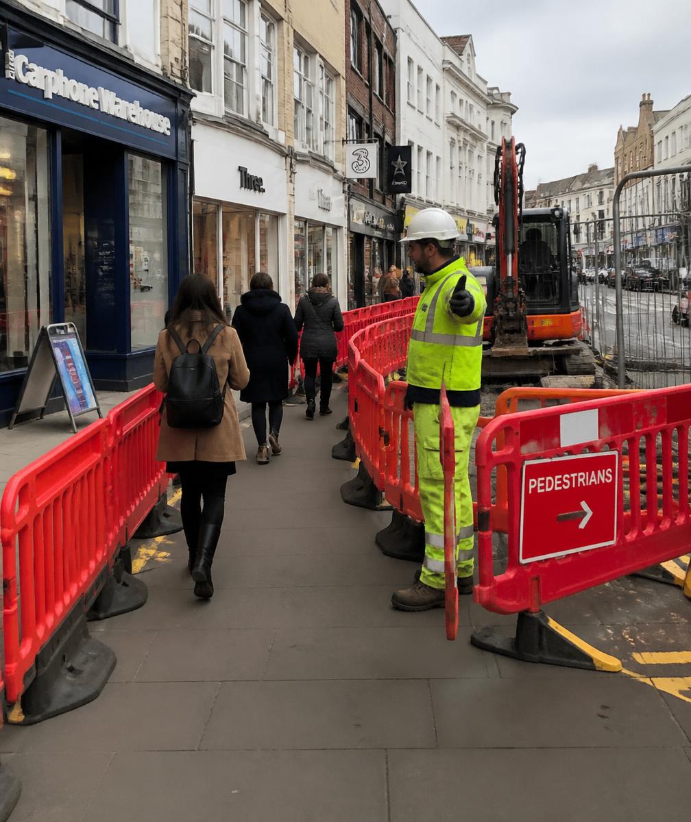 Managed pedestrian walkway with barriers past utility works on a high street
